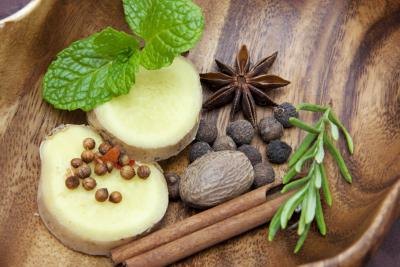 Fresh herbs and spices in a wooden bowl, including ginger, rosemary, cinnamon, nutmeg, mint, and anise.