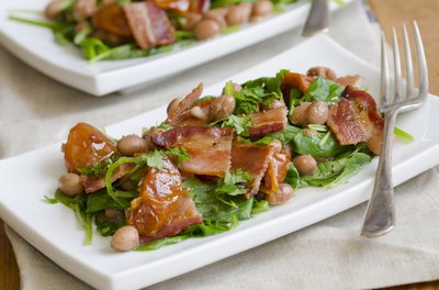 Two spinach salads topped with garbanzo beans and bacon.