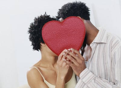 A man and woman are kissing behind a red heart.