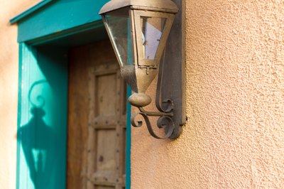 A close-up of a rustic light fixture next to a wooden door with turquoise trim on a stucco home.