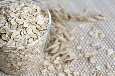 A glass cup filled with raw oat flakes.