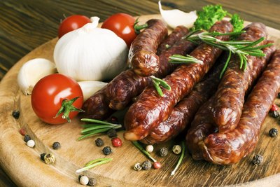 Pork sausages on a cutting board with onions and tomatoes.