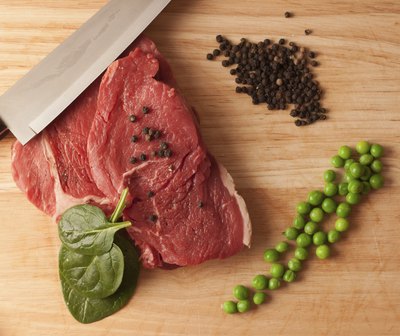 A overhead view of beef, spinach and peas on a cutting board.