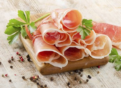 Sliced rolls of prosciutto on a wood serving tray.