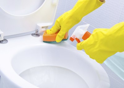 Close-up of two gloved hands cleaning toilet
