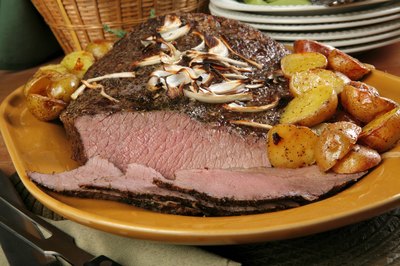 Slices of beef brisket on a plate with mushrooms and potatoes.