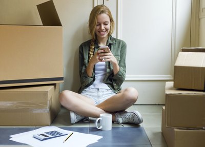 A woman sitting next to cardboard boxes while using her smartphone