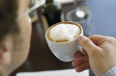 A man drinks a cappucino at a cafe.