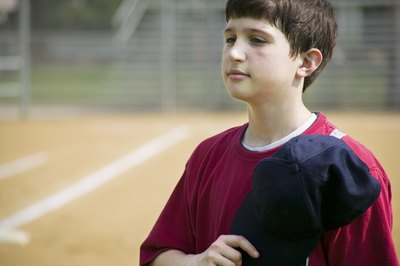 A young boy holds his baseball hat over his heart while singing the anthem