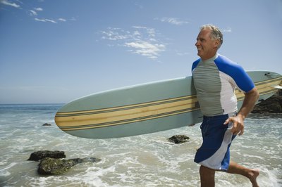 An older man run with a surfboard.