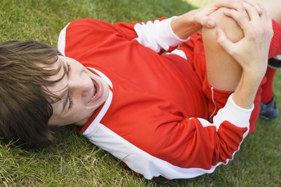A soccer player holds his knee in pain.