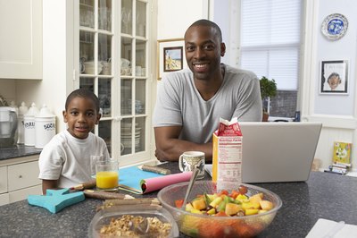 A man working on a laptop in the kitchen with his son