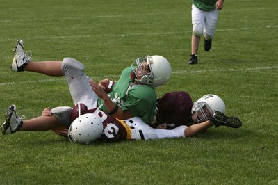 Three boys lay on the football field after a tackle.