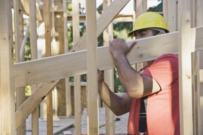 A man carries lumber in the frame of a house.