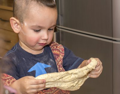 A tot streching out bread dough with his hands.