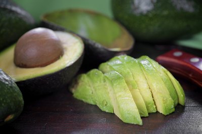A halved avocado next to avocado slices.