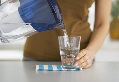 A woman pouring a glass of filtered water from a pitcher a the kitchen counter.