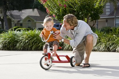 Dad helping child learn to ride a tricycle
