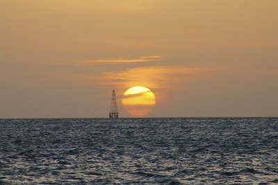 The silhouette of an oil rig on the horizon at sunset.