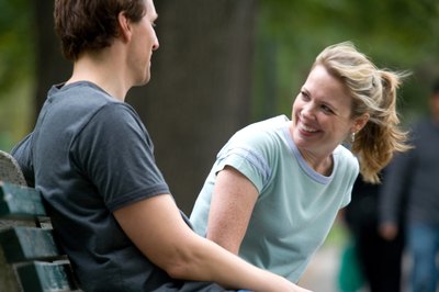 A couple smiles and converses on a park bench.