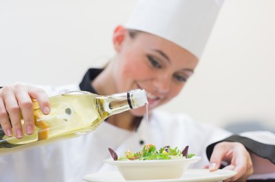 A cook adds oil to a salad.