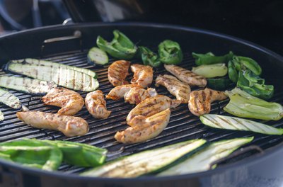 A grill with chicken and vegetables cooking.
