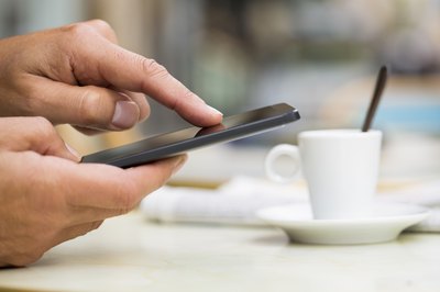 A man using his smart phone on a cafe terrace.