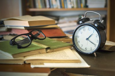 Vintage books, eye glasses, and clock on a desk.