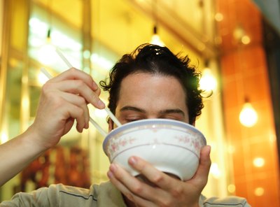 A close-up of a man eating noodle soup in a restaurant.