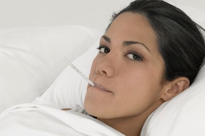 Young woman in bed with thermometer in mouth.