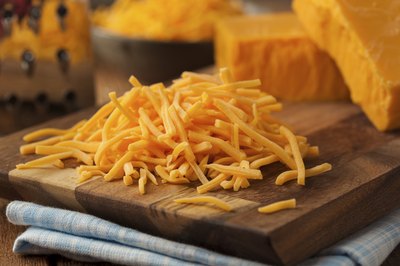 Shredded cheddar cheese on cutting board.