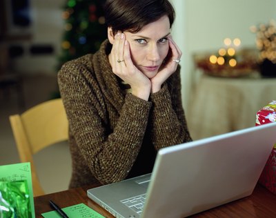 A woman rests her chin in her hands while looking at a laptop.