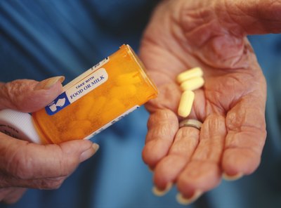 Senior woman putting pills in her hand.