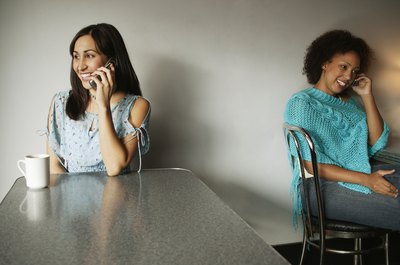 Two women talking on mobile phones in a coffeehouse.