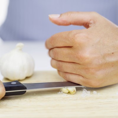 A woman crushes garlic with the side of a knife.