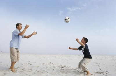 Father and son playing soccer on beach