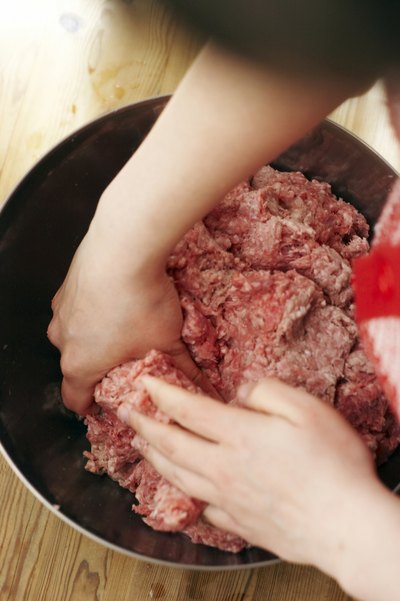 A close-up of a woman making a meatball mix with ground meat in a bowl.