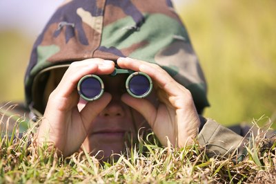 A soldier is laying in the field wearing camouflage.