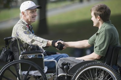 Young man in wheelchair shaking hand of veteran in wheelchair.