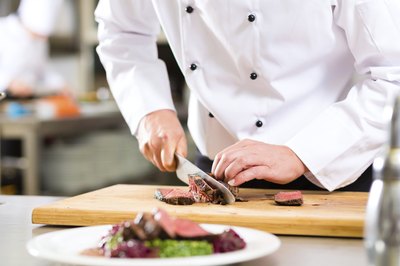Chef slicing steak behind a prepared plate.