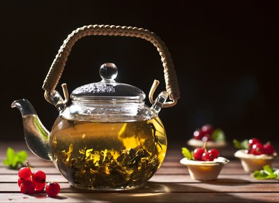 A teaport filled with green tea on a wooden table with garnishes