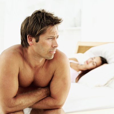 A man sits on a bed while his partner sleeps.