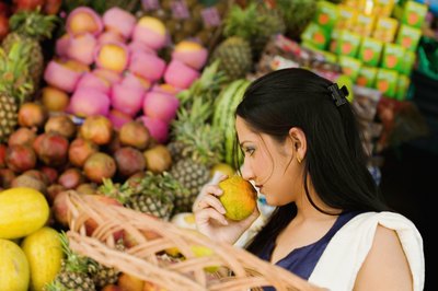 A woman is sniffing fruit in the supermarket.