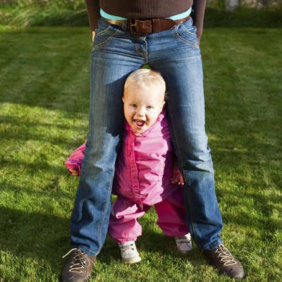 A toddler walks in between her mother's legs.