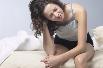 A woman who doesn't feel well sits on her bed.