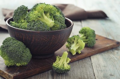 Broccoli in a bowl and on a wood table.