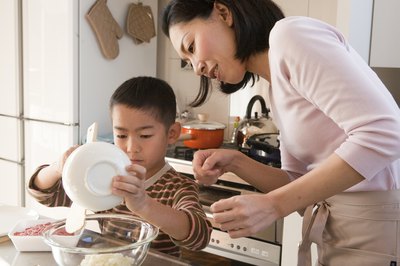 A mother helping her son add ingredients to a mixing bowl.