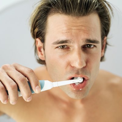 Portrait of a young man brushing teeth with an electric toothbrush.