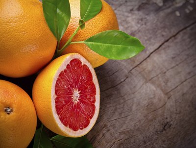 Whole and halved grapefruits on a wood surface.