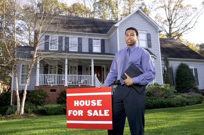 A young real estate agent standing next to a house for sale sign.